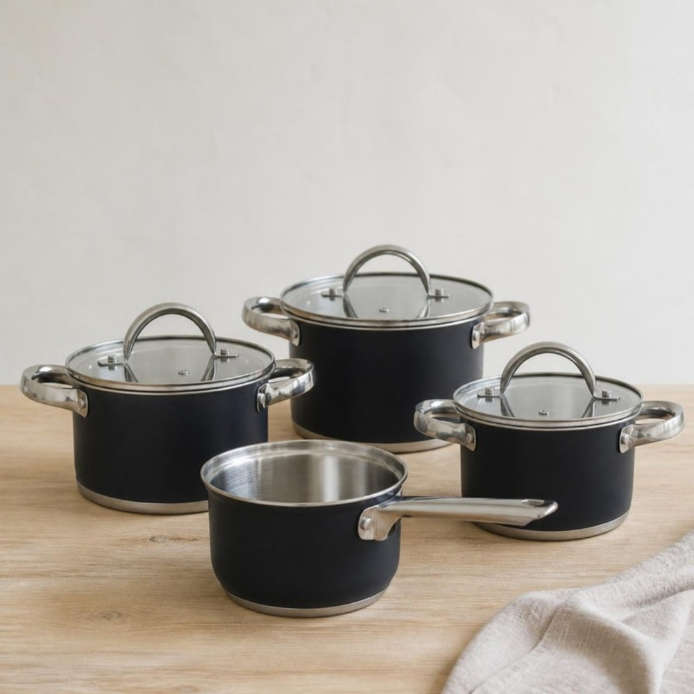 Cooking Pannenset Zwart 4-delig: drie zwarte kookpannen en een steelpan op een eiken werkblad